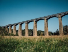 Looking up at a long aqueduct against a blue sky, with green grass in the foreground.