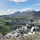 View of a town surrounded by slate waste with mountains in the background.
