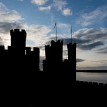 Silhouette of castle turrets and walls against a cloudy blue sky.