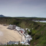 buildings on the beach, backing onto green hills.